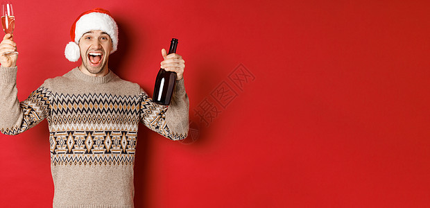 冬假 圣诞节和庆祝活动的概念 穿着毛衣和圣诞帽的英俊帅哥兴奋 享受新年晚会 举起玻璃和香槟酒瓶 玩得开心 喝 脸图片