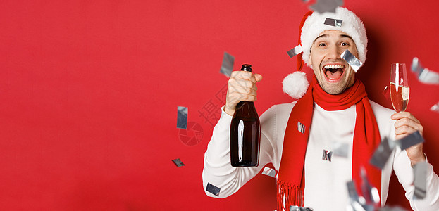 庆祝新年的快乐男人 拿着香槟瓶和杯子 用彩礼顶着红色背景站立在面团上 注 un org/docute_BAR__BAR_ 成人 图片