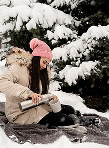 穿着温暖冬衣的漂亮女人 拿着热温水和在雪天户外喝热茶或咖啡 公园 闲暇图片