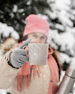 穿着冬衣的女子在雪天露户带杯子和热茶或咖啡图片