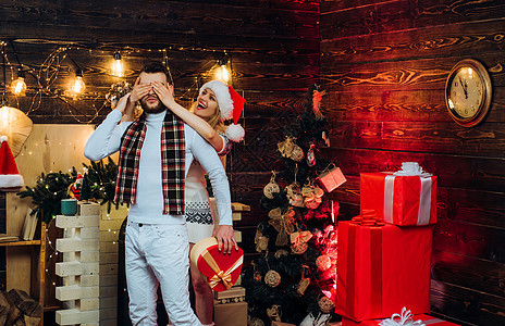 快乐的女朋友用手捂住眼睛 为男友准备圣诞惊喜 礼盒 新年假期的全装修内饰 一起庆祝圣诞节的概念图片