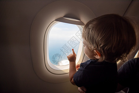 恢复航班 开放边界概念 一个小孩从一架飞行的飞机的窗口看着大海 第一次飞行 假期快乐 女孩 童年图片