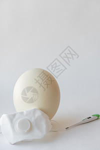 在呼吸器和温度计中的大白色复活节鸵鸟蛋 鸡蛋 呼吸器和温度计 复活节和冠状病毒 Covid-19 白色背景的鸵鸟蛋 医用面具和温图片