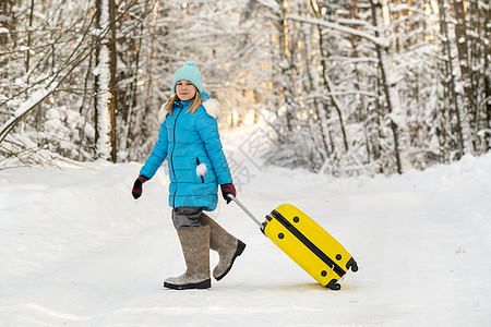 在寒冷的雪天 一个身穿脚靴的冬天女孩 带着手提箱去 行李 蓝色夹克图片