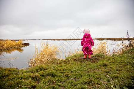 一个小孩站在湖的岸边 看着远处 幼儿在冬季西装 后视中行走着自然体 冬天 孩子图片