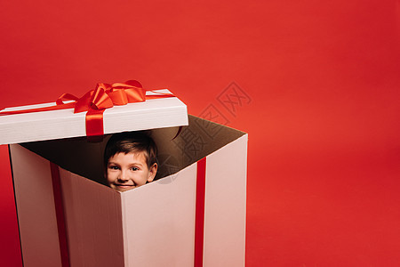 一个小男孩坐在圣诞礼物上 看着红色背景的红色外表 男生 微笑图片