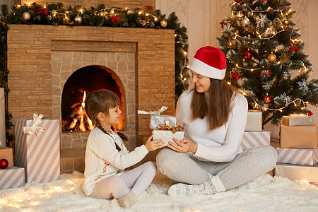 圣诞节早上 年轻女子在客厅里从她留着两条辫子的可爱小女儿那里得到圣诞礼物 庆祝圣诞节和新年 一起度过快乐 快乐的时光图片