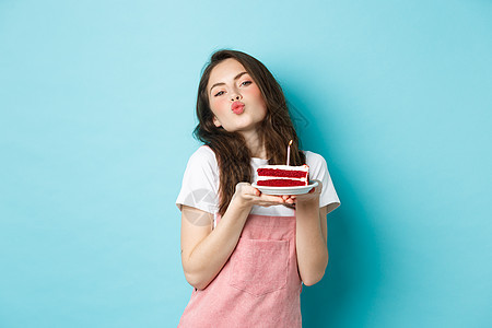 节日和庆祝活动 可爱的傻女孩在生日蛋糕上许愿 亲吻脸 庆祝生日 在蓝色背景下欢快地站着 漂亮的 情绪图片
