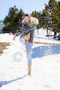 年轻快乐的女士 在山上一片雪覆盖的森林里踢雪 毛茸茸的 女性图片