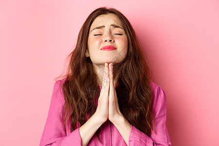 年轻女子恳求上帝的特写 手牵着手祈祷 闭着眼睛 满脸希望 乞求帮助 站在粉红色的背景下 快乐 快乐的图片