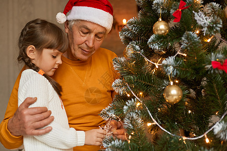 一家人在家庆祝圣诞节 爷爷和孙子一起装饰圣诞树 看起来很专注 穿着休闲服装 戴着圣诞老人帽子的成熟男人图片