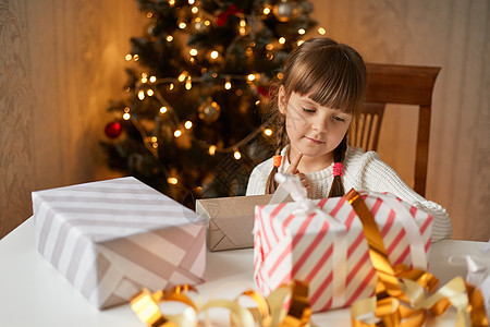 迷人的孩子在节日房间里打包圣诞礼物 看着盒子 穿着休闲装 留着黑头发和两条辫子 为新年树准备礼物图片