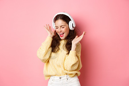 快乐女孩唱着最喜爱的歌 用无线耳机听音乐 微笑和跳舞 站在粉红背景上 可爱的 高兴图片