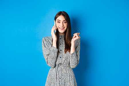 激动人心的女性在手机上收到好消息 微笑快乐 用智能电话交谈 站在蓝背景上;以及 移动的 假期图片