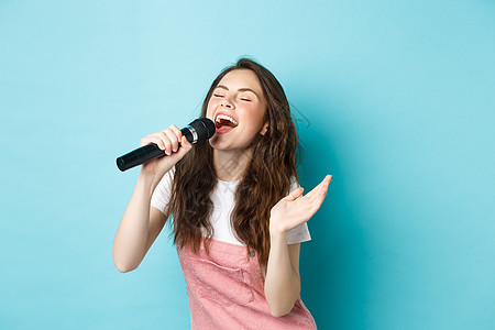 无忧无虑的美丽美女演唱歌曲 用麦克风和激情歌唱 玩卡拉OK 站在蓝背景上 假期 情绪图片
