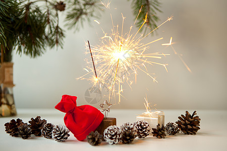 女人手在松果 圣诞树和红色圣诞帽附近点燃节日的火花 新年晚会在白色背景上燃烧烟火特写 烟花 闪耀的火焰 圣诞灯图片