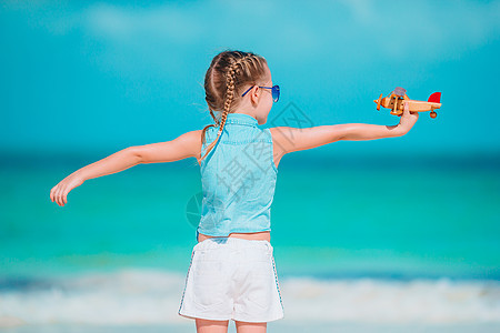 带玩具飞机的快乐小女孩 在白沙滩上手握着玩具飞机 快乐的 微笑图片