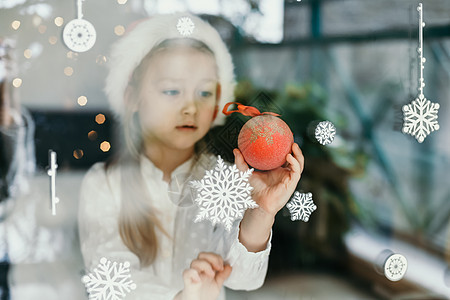 一个戴着圣塔克拉斯帽的女孩 看着窗户上的雪花 冬天图片