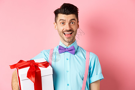 假期和庆祝活动的概念 身着节日服装的快乐年轻人拿着大礼盒过生日 欢快地站着 微笑着 粉红色的背景 胡子 工作室图片