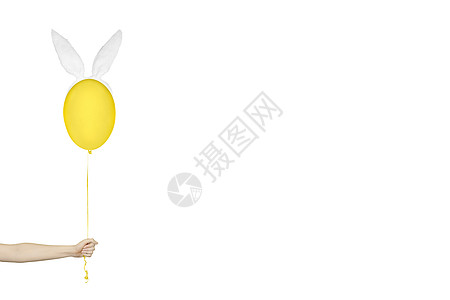 创意复活节最小概念 手拿着一个黄色气球 兔子耳朵上白色孤立 带复制空间的单色横幅图片