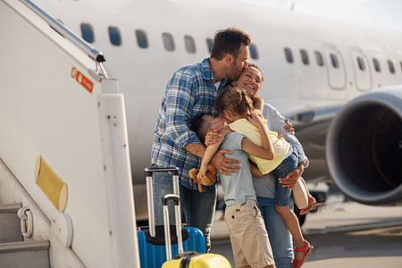 四口子四口亲吻的一家人 一起出去旅行 站在户外大飞机前图片