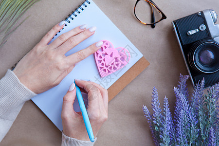 木心的爱和女人把手放在桌上的笔记本和复古相机后面 信件写作概念 心形符号 情人节-浪漫问候生活方式感受概念 眼镜 线条图片