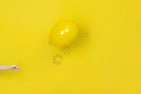 女性手持飞行的黄色气球 派对或现在的概念 黄色气球和孤立在黄色背景上的手 带有复制空间的单色横幅图片