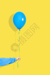 女手拿着蓝色气球 派对或现在的概念 黄色背景上孤立的蓝色连帽衫的蓝色气球和手图片