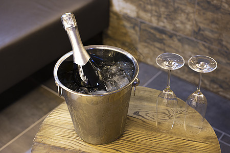 香槟瓶装在冷却器里 有冰的桶子和木制桌子上的两杯香槟杯 浪漫晚餐和派对概念图片