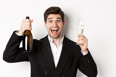 穿着黑色西装的英俊微笑男子的特写镜头 敬酒 拿着香槟和玻璃杯 庆祝新年 站在白色背景下 圣诞节 圣诞节快乐图片