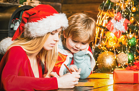 年轻的母亲和儿子给圣诞老人写了一封信 寒假和童年的概念 圣诞老人的助手与圣诞老人的愿望清单图片