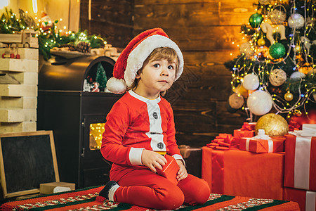 可爱的小男孩圣诞老人 圣诞背景上有新年礼物 精灵小孩 在火场的寒假礼物背景图片