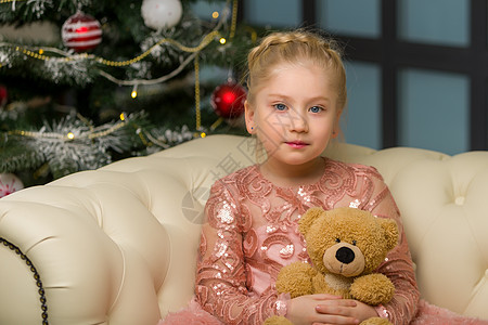 一个小姑娘带着泰迪熊坐在 圣诞树附近的沙发上 圣诞老人 裙子图片