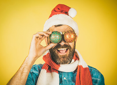 圣塔帽和围巾上的圣诞潮人快乐笑容 黄色背景的男子用Xma球遮住眼睛图片