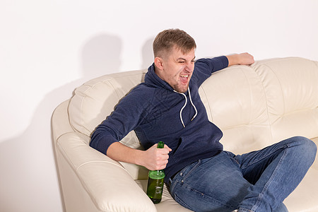 抑郁症和酗酒概念   激进的青年男子坐在沙发上 喝着酒 白色的 啤酒图片