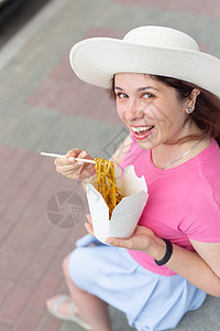 身戴帽子的年轻女子在温暖的夏天在公园散步时吃中国面条 外送食物概念 笑声 乌冬面 闲暇图片
