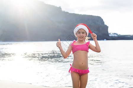 沙滩上戴着红帽圣诞老人的可爱小女孩 新年 童年图片
