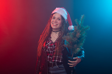 圣诞节 摇滚 工作室 人的概念 — 戴着圣诞帽 深色背景上挂着小圣诞树的年轻女性 美丽 蓝色的图片