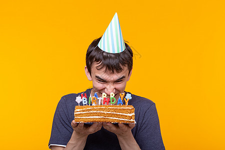 戴眼镜的有趣积极的家伙手里拿着一个自制的蛋糕 上面写着生日快乐 背景是黄色的 假期和周年纪念日的概念 派对 幸福图片