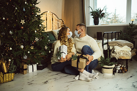 情侣相爱 坐在圣诞树附近 家里有礼物盒图片