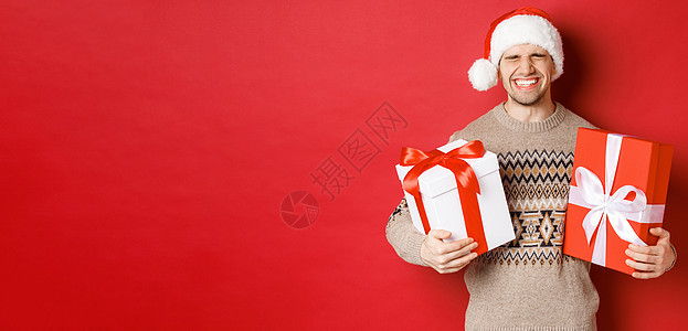 寒假 新年和庆祝活动的概念 快乐而兴奋的年轻人喜欢礼物 拿着礼物 微笑着 戴着圣诞帽和圣诞毛衣 广告 圣诞节快乐图片