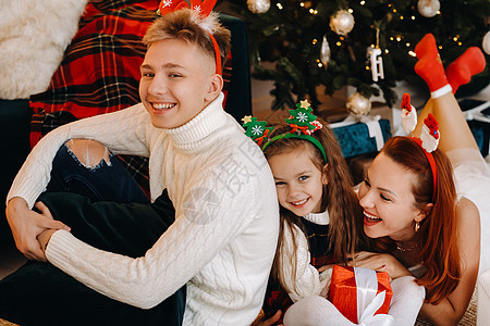 一个幸福的家庭躺在房子的地板上 旁边是圣诞树 上面放着新年礼物 灯 男生背景图片