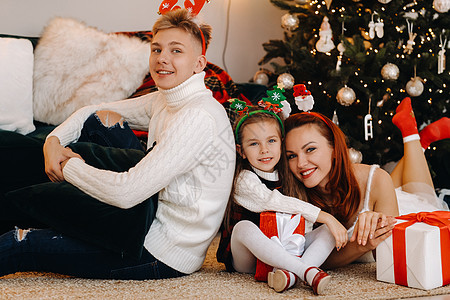 一个幸福的家庭躺在房子的地板上 旁边是圣诞树 上面放着新年礼物 家庭价值观 快乐的背景图片