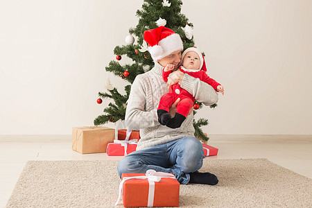 父亲带着他的男婴戴着圣诞老人的帽子庆祝圣诞节 温暖的 乐趣图片