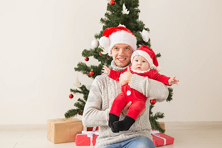 父亲带着他的男婴戴着圣诞老人的帽子庆祝圣诞节 关心 快乐的图片