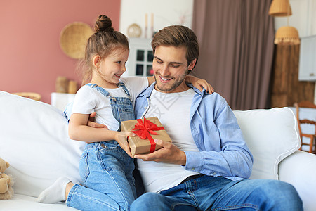 可爱的小女儿给爸爸惊喜 小女孩把礼盒送给坐在沙发上的爸爸 父亲节 幼儿园 假期图片