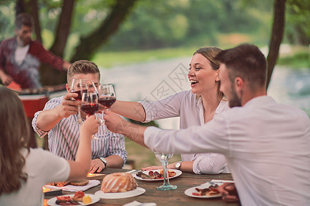 朋友们在野餐晚宴上 烤红酒杯 边吃野餐 生日图片