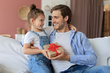 可爱的小女儿给爸爸惊喜 小女孩把礼盒送给坐在沙发上的爸爸 父亲节 笑 幼儿园图片