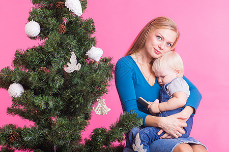 假日 家庭和圣诞节概念   年青妇女 带着婴儿在圣诞树附近的粉红背景上 壁炉 团聚图片