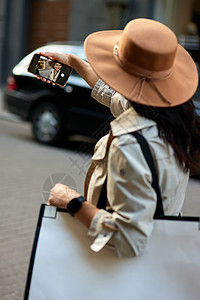 看着一个年轻时尚女性的景象 她穿着大购物袋在街上散步时用智能手机做自拍图片